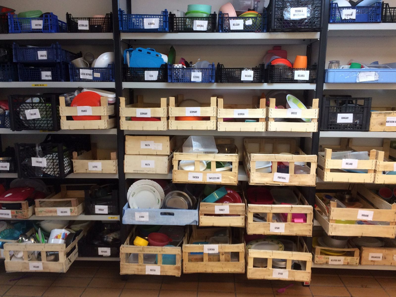 Festival Feed: shelves of wooden and plastic crates, one per country, holding each EASA team’s own plates and tableware
