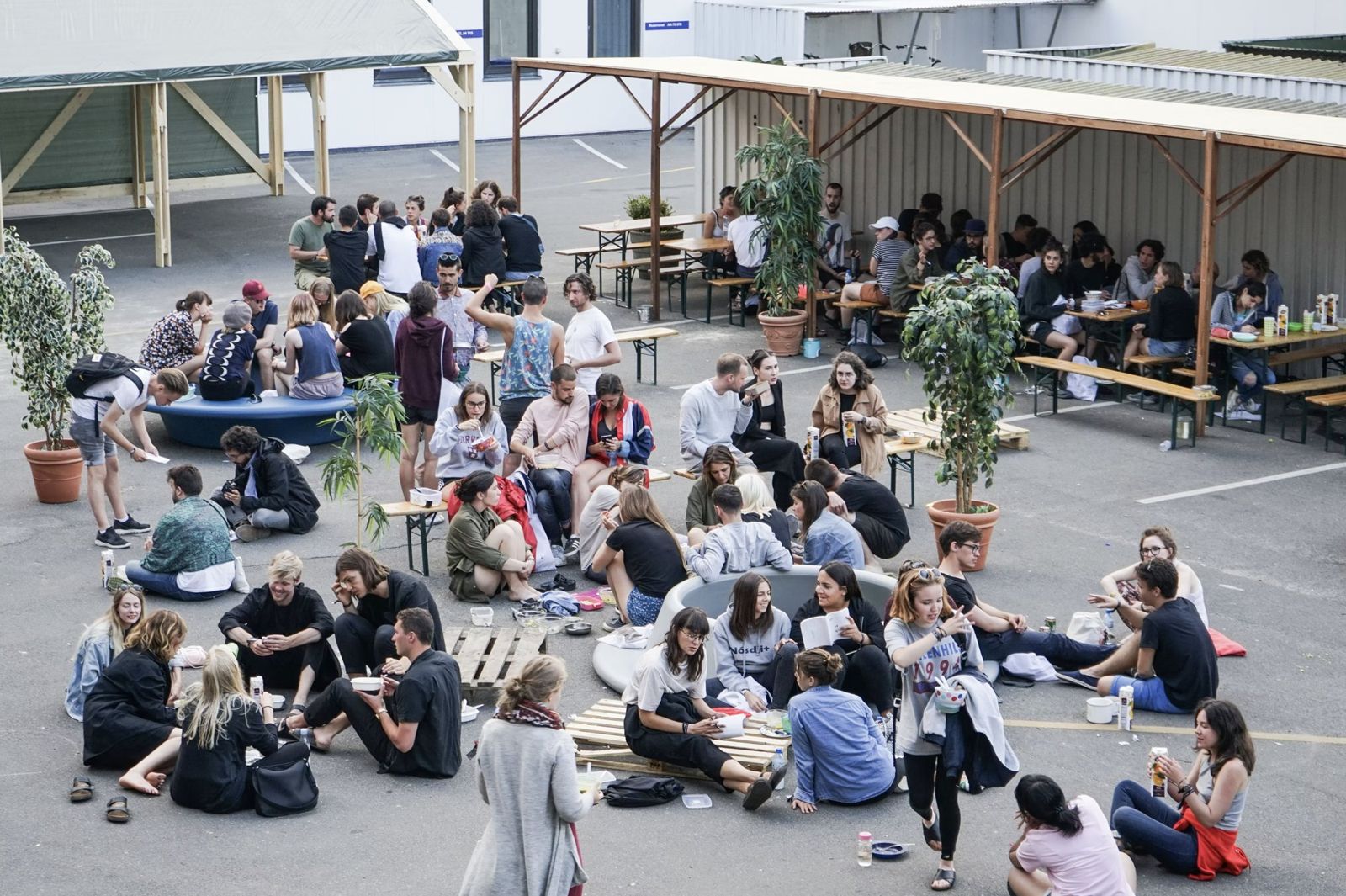 Festival participants eating together on benches, pallets and the ground in the courtyard
