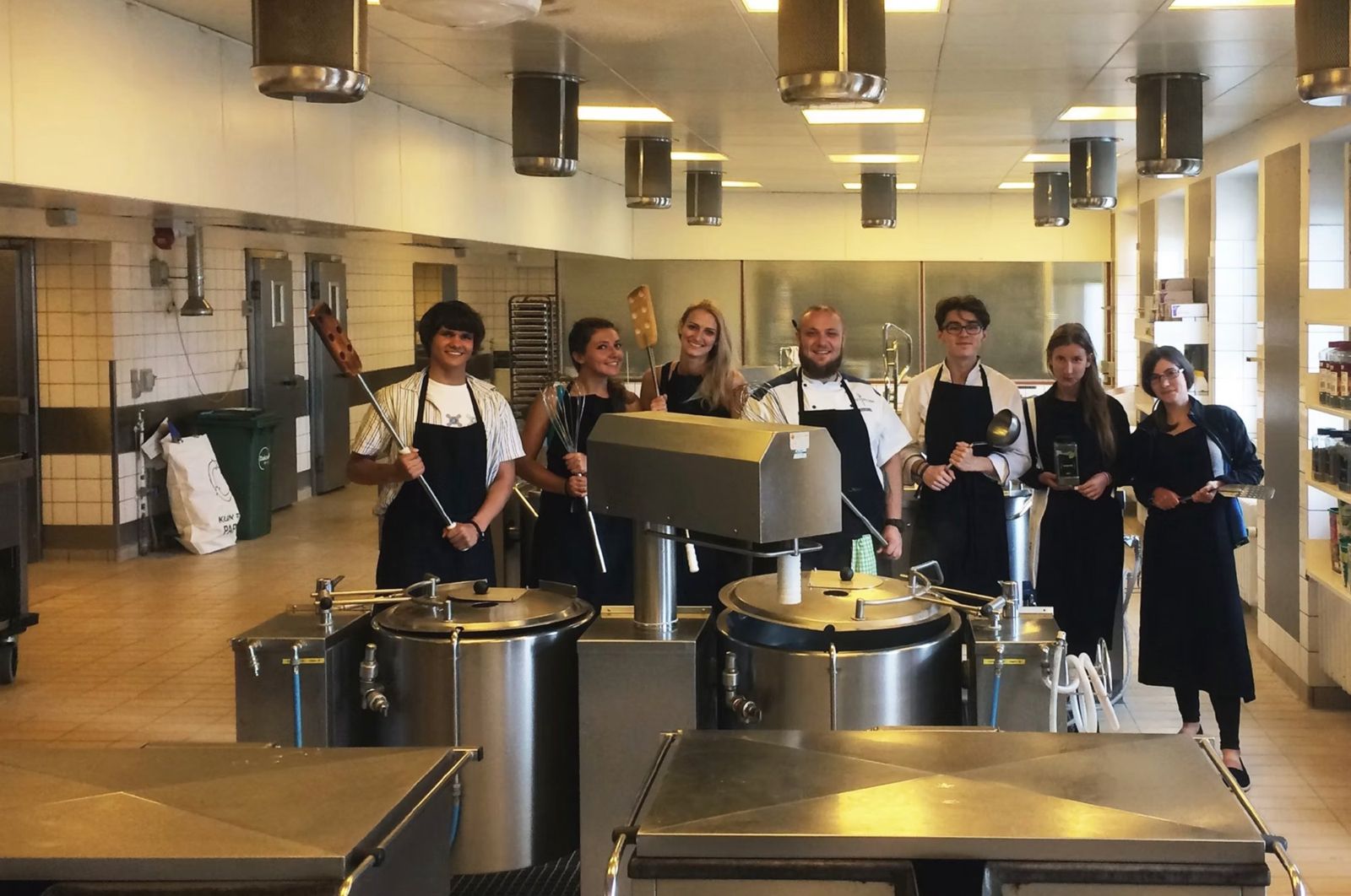 The food team with the chef in the industrial kitchen, holding oversized cooking utensils