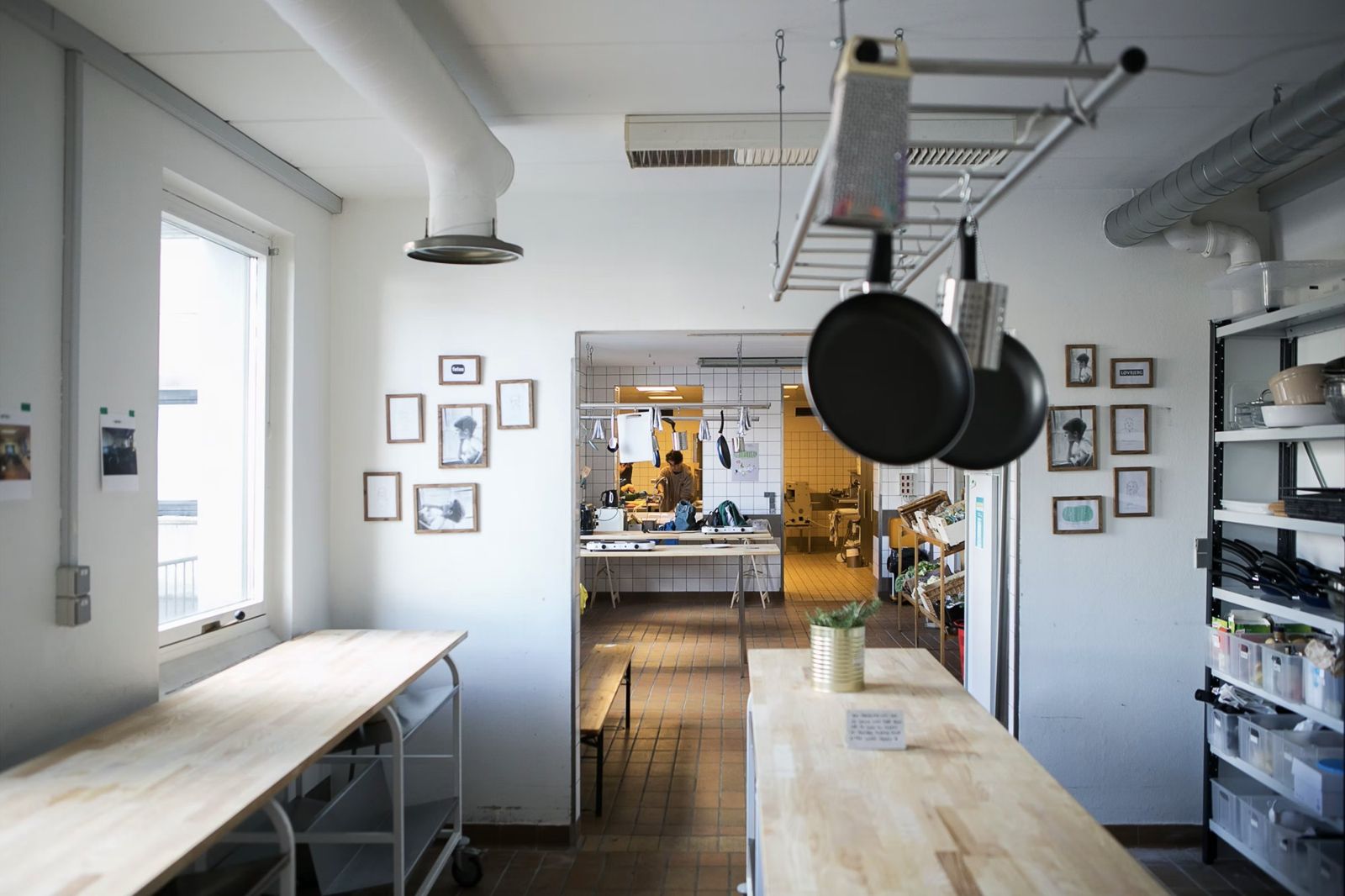 Fredericia Food Lab dining room with wooden tables, framed portraits and a view through to the tiled kitchen