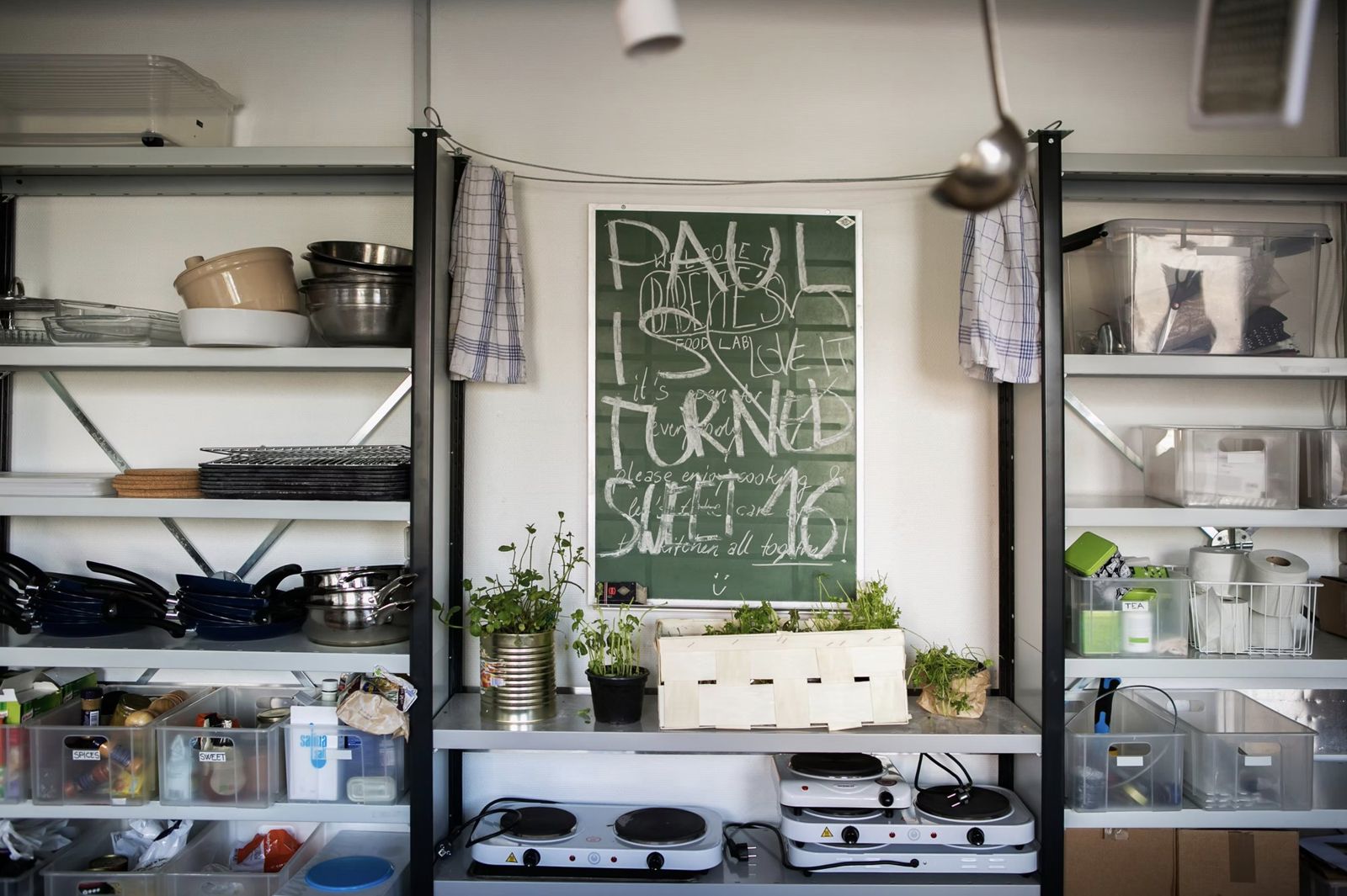 Shelving with pans, herbs and hot plates around a chalkboard in the Fredericia Food Lab